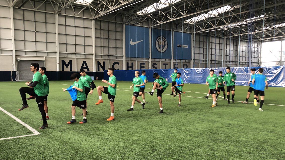 Young footballers in green kit training at a Manchester City indoor football facility