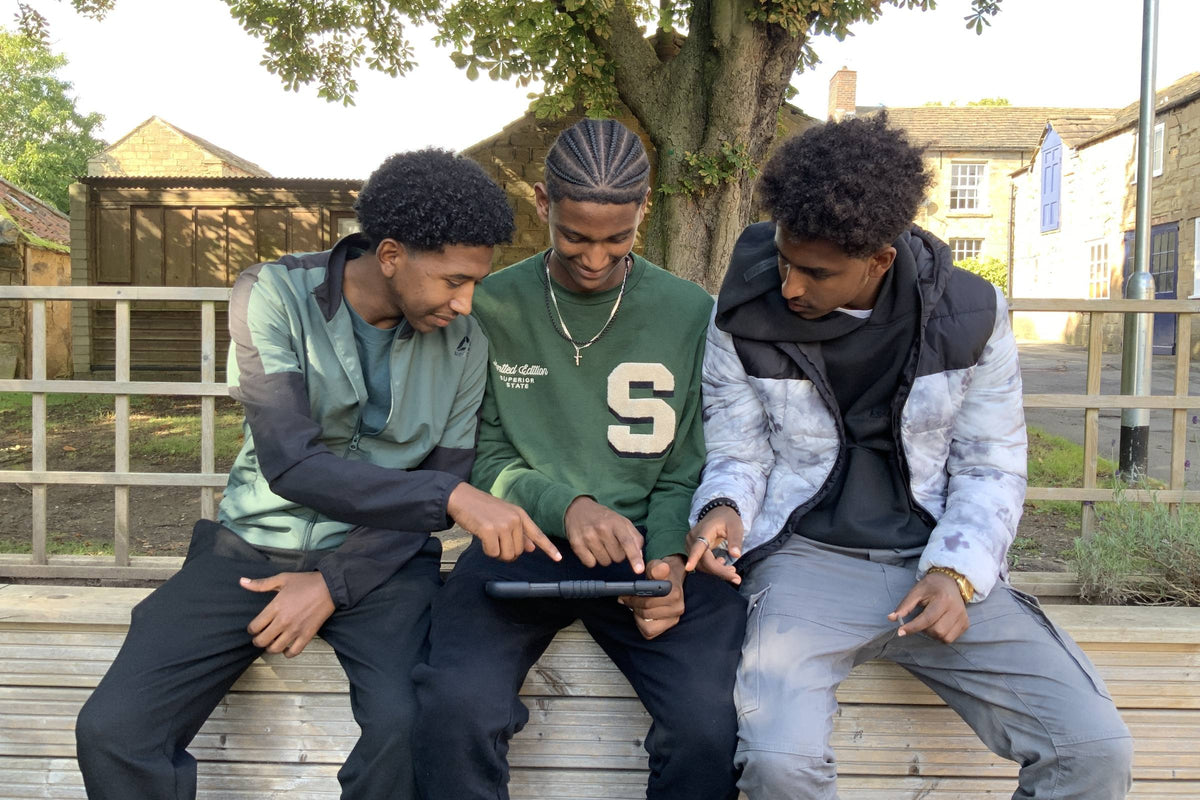 Three sixth-form students looking at a tablet together on a bench at a UK school